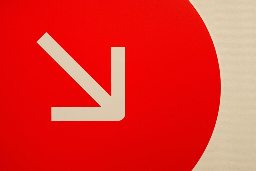 A minimalist image of a white downward arrow on a red round background, conveying direction and simplicity.